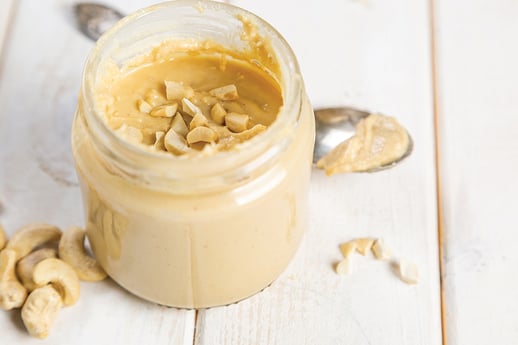 A jar of cashew butter with crushed cashews on the top.